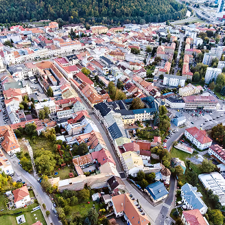 Luftaufnahme einer Stadt mit Wohnhäusern, Straßen und Bäumen, umgeben von grünen Hügeln.